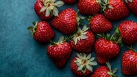Fresh ripe strawberries scattered on dark turquoise background, macro shot showing detailed texture and natural green leaves, dramatic food photography.