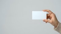 Hand holding blank white business card against neutral gray background, suitable for branding, corporate identity, and marketing mockup designs.