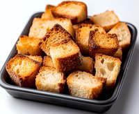 Crispy golden croutons made from toasted bread cubes in black serving dish, close up view showing crunchy texture and airy interior structure.