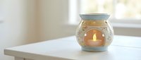 Lit candle in decorative glass holder on white table by window, creating warm ambient light for home decor and relaxation.