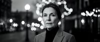 Professional middle-aged Caucasian businesswoman in suit standing outdoors at night with bokeh city lights creating atmospheric urban portrait for corporate use.