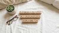Wooden letter blocks spelling community kindness growth on white bedding with glasses and succulent plant for motivational lifestyle content.