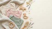 Flat lay of organic baby clothes in neutral colors with wooden toys and natural accessories on beige background for newborn care and parenting.