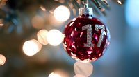 Red glass Christmas ball ornament with number 17 in silver glitter hanging on tree branch with soft bokeh lights creating festive holiday atmosphere.
