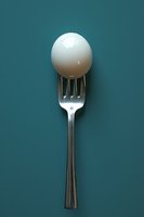 White egg balanced on silver fork against teal background, minimalist food photography composition showing culinary creativity and balance.