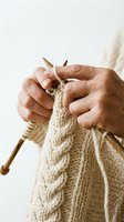 Mature hands knitting a cable pattern sweater with wooden needles and cream wool yarn, showcasing traditional handcraft and cozy textile artistry.