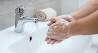 Hands washing with soap under running water from modern chrome faucet in white bathroom sink. Personal hygiene and cleanliness routine for health protection.