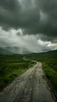 Winding dirt road cuts through lush green valley under dramatic stormy sky with rain falling on distant mountains, conveying isolation and adventure.