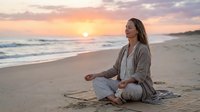 Young woman meditating on beach at sunrise, peaceful morning yoga practice on sandy shore with ocean waves and golden sky, wellness and mindfulness concept.