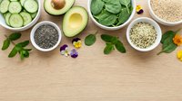 Fresh healthy ingredients including sliced cucumber, avocado, spinach leaves, chia seeds, quinoa and hemp seeds arranged on wooden background for smoothie preparation.