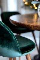 Modern dining room interior with emerald green velvet chair and wooden table, soft bokeh lights in background creating luxurious atmosphere.