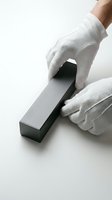 Hands in white cotton gloves carefully handling black rectangular object on clean white surface for professional product photography and luxury presentation.