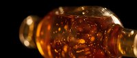 Amber liquid pouring from glass bottle against dark background, suitable for beverage, alcohol, and product photography projects.