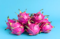 Fresh dragon fruit arranged in group showing vibrant pink exterior and green scales against blue background, natural tropical produce photography.