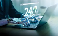 Robotic hand typing on laptop with glowing 24/7 service hologram display for automated customer support and AI assistance technology concepts.