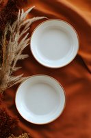 Empty white porcelain plates with gold trim on brown silk background decorated with dried pampas grass and flowers, modern minimalist table setting composition.