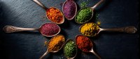 Colorful spices and herbs in wooden spoons arranged in circle on dark slate background for cooking and seasoning culinary ingredients kitchen preparation.