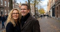Happy mature couple embracing on cobblestone street in historic European city center during autumn day with warm sunlight and pedestrians in background.