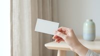 Female hand holding blank white business card mockup in modern minimalist interior with soft natural lighting for branding presentation.