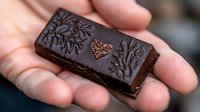 Artisan dark chocolate bar with embossed floral pattern and heart design held in cupped hands, premium confectionery treat for gourmet food photography.