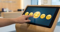 Customer feedback rating system with hand selecting emoji faces on tablet screen for service evaluation and satisfaction survey in modern office environment.