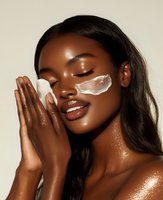 Young African American woman with glowing skin wearing under-eye patches and shimmering highlighter in peaceful spa pose, demonstrating skincare and beauty routine.