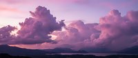 Dramatic purple and pink sunset clouds over mountain landscape with vibrant sky colors creating peaceful evening atmosphere for nature backgrounds.