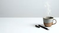 Minimalist workspace with ceramic coffee mug and black pens on white desk. Clean modern office setup for productivity and creative work.
