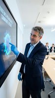 Middle-aged Caucasian businessman in dark suit and blue gloves interacting with futuristic holographic display in modern office conference room setting.