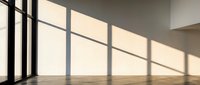 Empty modern interior room with large windows casting geometric shadows on wooden floor and white walls creating minimalist architectural space.