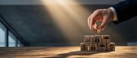 Businessman hand placing wooden cube with house icon on blocks spelling MORTGAGE, representing home loan and real estate financing concepts.