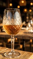 Crystal cut wine glass filled with amber whiskey on wooden table with warm bokeh lights creating elegant bar atmosphere for luxury dining concepts.