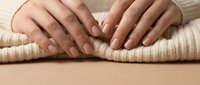 Woman hands with nude manicure on knitted sweater fabric showing natural nail care and cozy winter fashion style for beauty and wellness concepts.