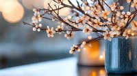 Delicate white cherry blossoms in blue ceramic vase against blurred bokeh background, creating cozy spring atmosphere with soft warm lighting effects.
