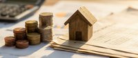 Small wooden house model with stacked coins on financial documents representing mortgage, real estate investment, property savings and home loan planning.