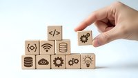 Hand placing wooden cube with gear icon completing technology stack of programming symbols including code brackets wifi database and lightbulb.