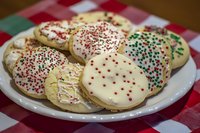 Decorated sugar cookies with red and green sprinkles arranged on white plate over checkered tablecloth, ready for holiday celebrations and festive gatherings.