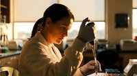 Female scientist in white lab coat conducting research with pipette in modern laboratory during golden hour lighting for scientific and medical content.