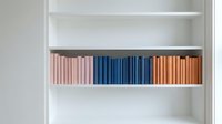 Colorful books arranged on white bookshelf with pink blue and orange spines creating organized library display for home office interior design.
