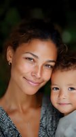 Mixed race mother and young son share tender moment outdoors, expressing genuine joy and connection against natural background. Authentic family lifestyle portrait.