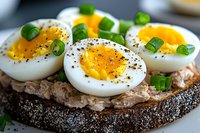 Sliced hard-boiled eggs with black pepper and green onions on whole grain bread, healthy breakfast or snack option for nutritious meal preparation.
