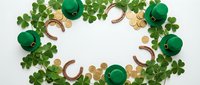 St Patrick's day flat lay with green leprechaun hats, horseshoes, gold coins and clover leaves arranged in circle on white background for holiday celebrations.