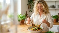 Young blonde woman enjoying healthy salad meal in bright modern kitchen with plants and natural lighting for wellness lifestyle content.