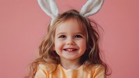 Happy little girl with bunny ears smiling on pink background for Easter celebration and spring holiday festivities.