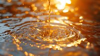 Golden liquid stream creating circular ripples on water surface with glowing bokeh lights and splash droplets in warm sunset colors. Macro photography.
