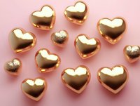 Golden metallic hearts scattered on pink background create romantic composition with reflection and shine, suitable for Valentine's Day designs and love themes.