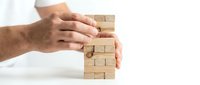 Male hands protecting wooden block tower on white background symbolizing business protection and risk management strategy.