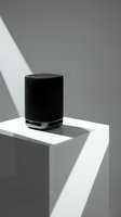 Black cylindrical smart speaker on white geometric podium with dramatic lighting and shadows for modern technology presentations.