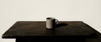 Minimalist composition featuring a cream-colored ceramic mug on a dark wooden table against a neutral background, suitable for lifestyle and product design projects.