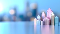 Miniature paper city skyline with pink and blue buildings on reflective surface against blurred urban background. Modern architectural concept for real estate.